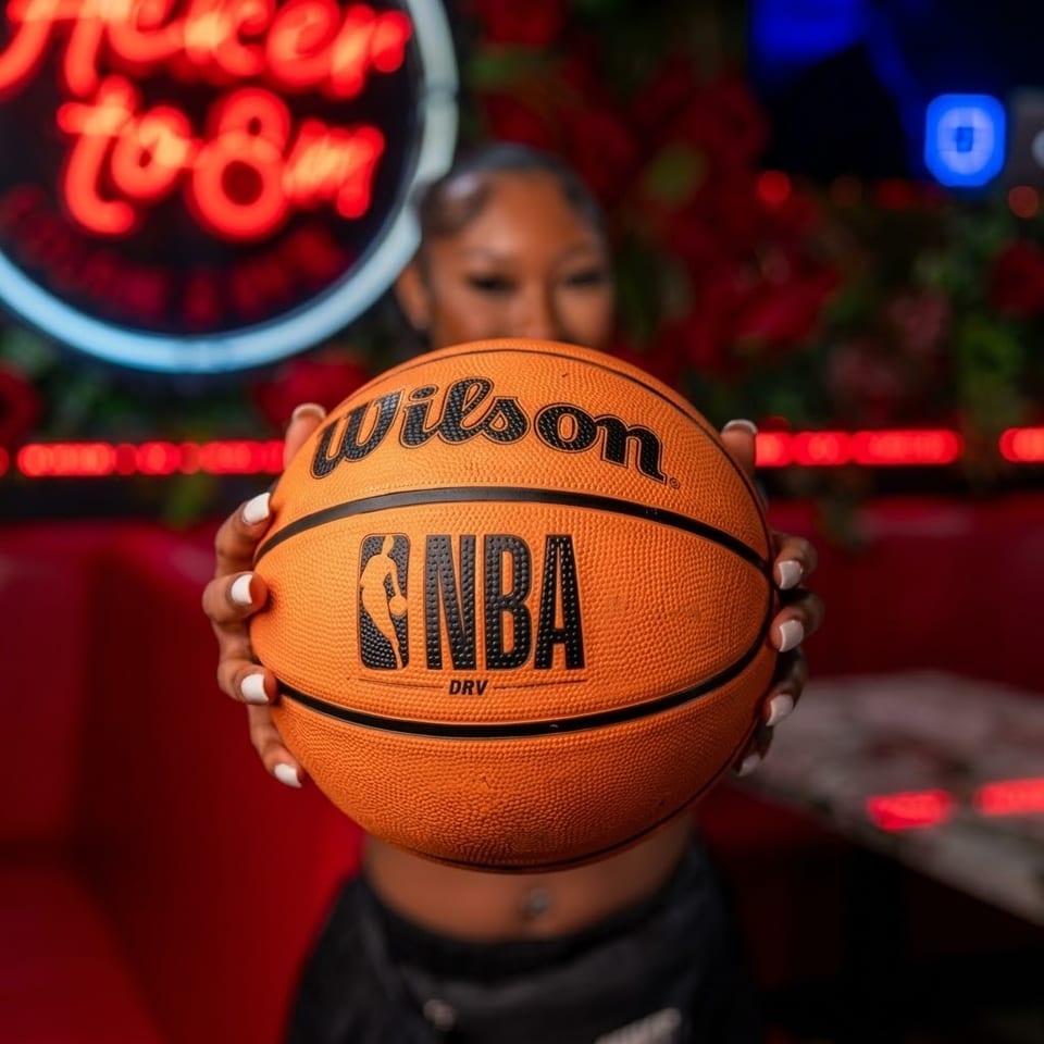 Person holding a Wilson NBA basketball in front of vibrant red and blue neon lights.