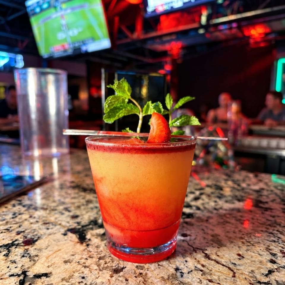 Strawberry cocktail garnished with fresh mint on a granite bar in a vibrant sports bar.